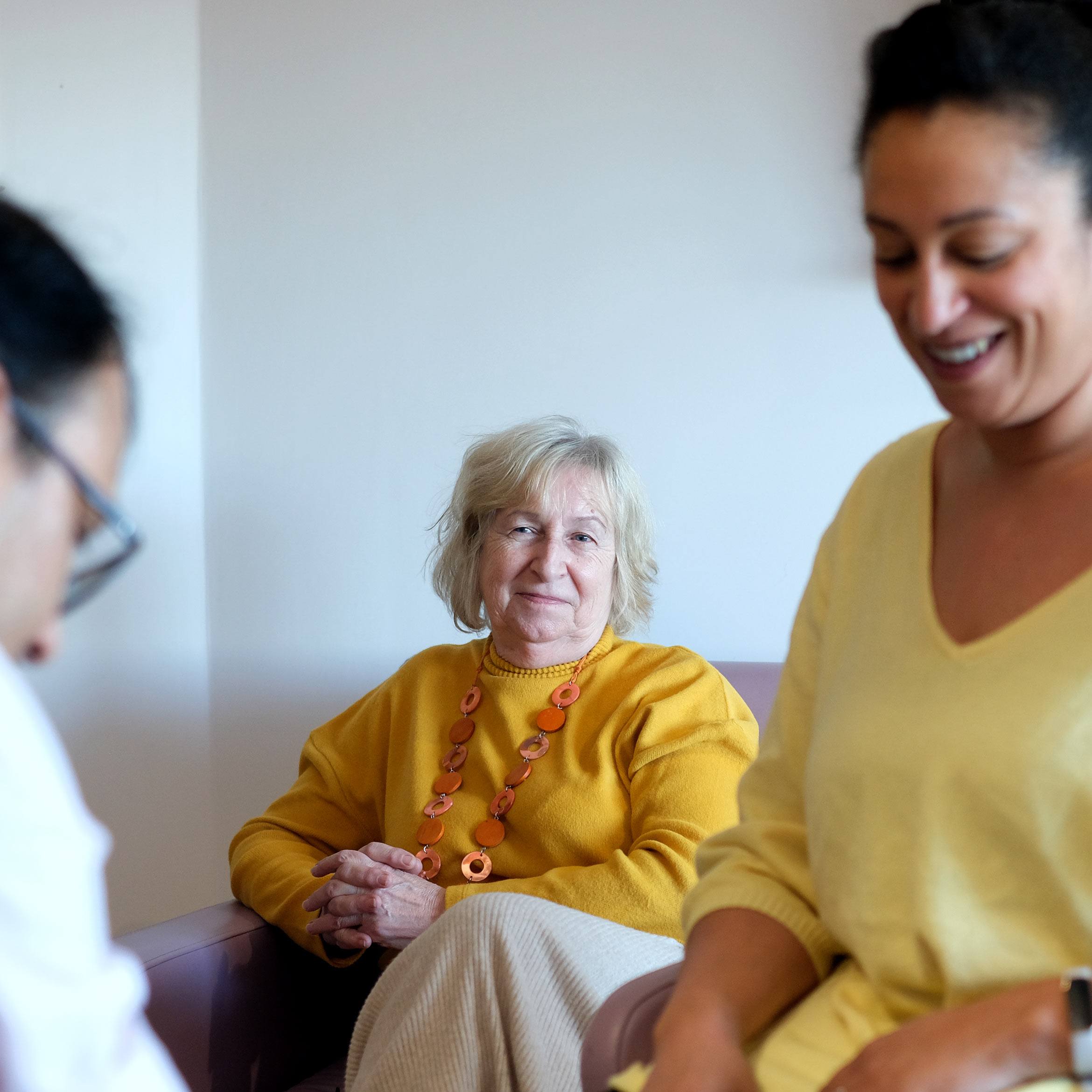 older-woman-sitting-down-watching-as-patient-and-doctor-speak